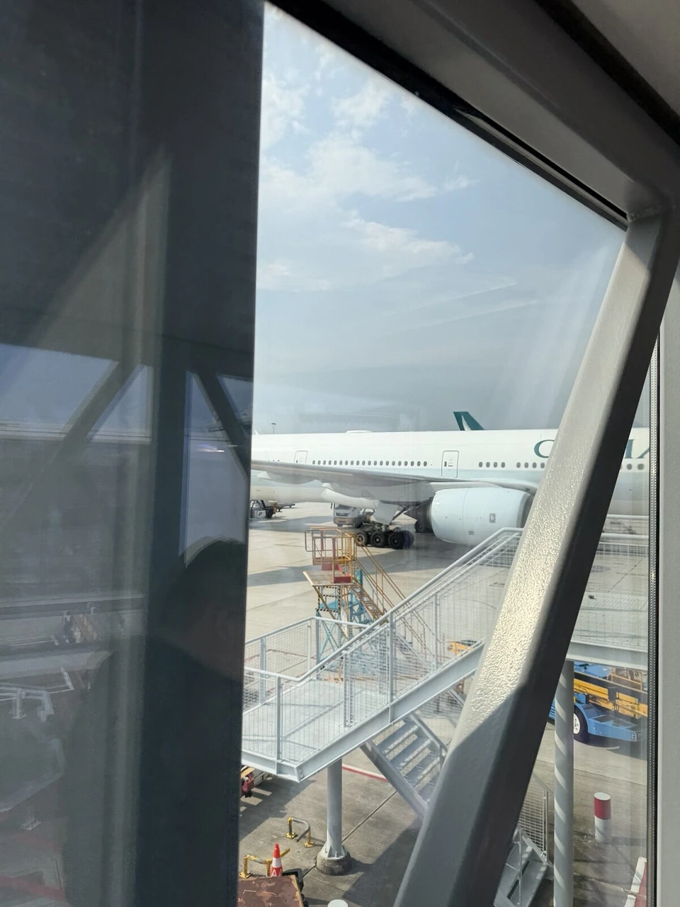 香港国際空港の窓の外に止まるキャセイパシフィック航空の機体と、搭乗橋の階段