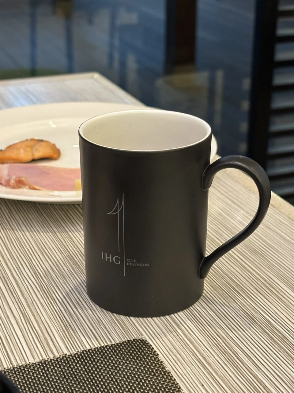 ANAクラウンプラザホテル福岡の朝食の席に置かれた、IHG ONE REWARDSのロゴ入りの黒いマグカップ