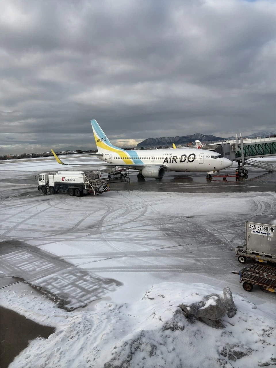 雪の積もった函館空港の駐機場に止まるAIRDOの機体。奥に函館山が見える