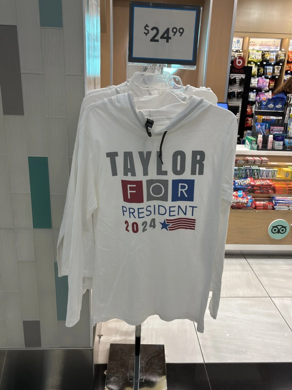 空港の売店に吊るされた白いパーカー。TAYLOR FOR PRESIDENT 2024の文字と24.99ドルの値札