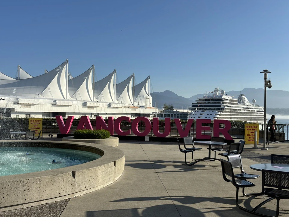 カナダプレイスの白い帆の屋根と、VANCOUVERの赤い文字のモニュメント。奥にクルーズ船