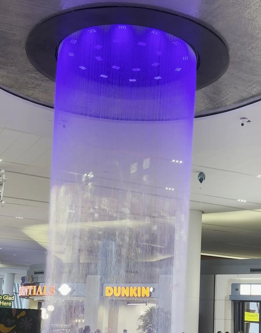 ラガーディア空港のターミナルの天井から、紫のライトに照らされて円柱のように落ちる噴水の水