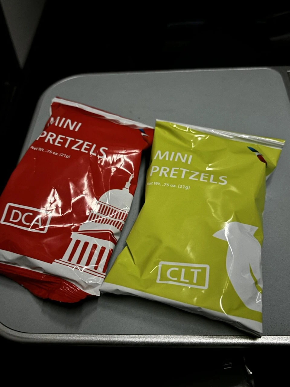 機内のテーブルに置かれた赤と黄緑のミニプレッツェルの袋