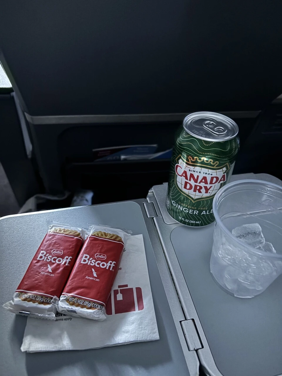 AA345の機内。テーブルにビスコフのクッキー2袋とカナダドライのジンジャーエール