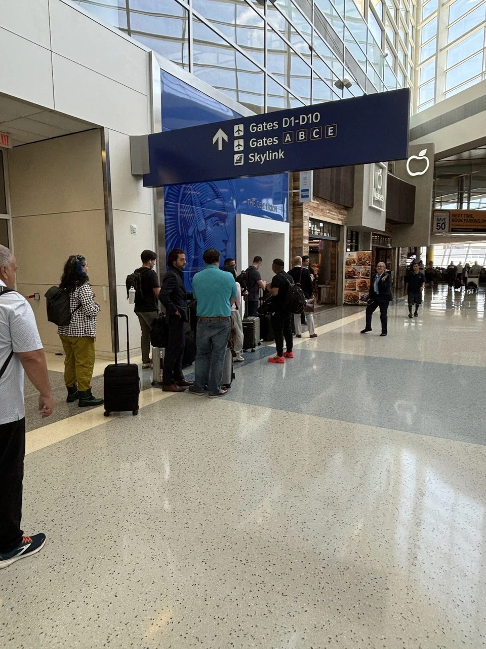 ダラス空港ターミナルDの明るい通路。Gates D1-D10とSkylinkの案内板