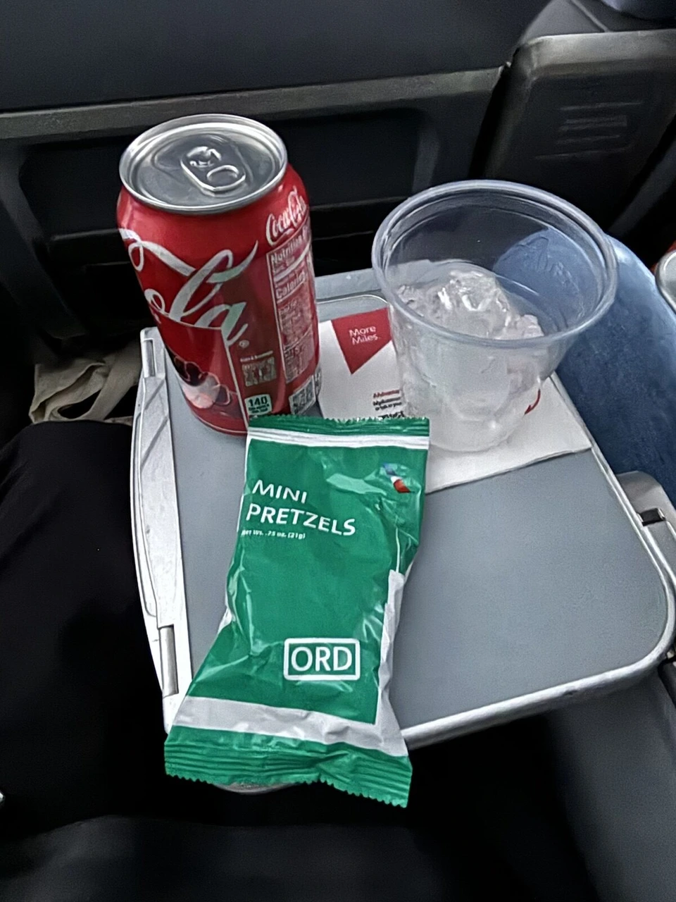 AA1456の機内。テーブルにコカ・コーラの缶とミニプレッツェルの袋