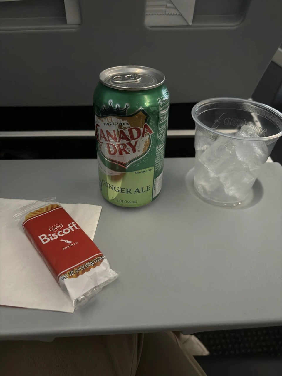 AA1214の機内。テーブルにカナダドライとビスコフのクッキー