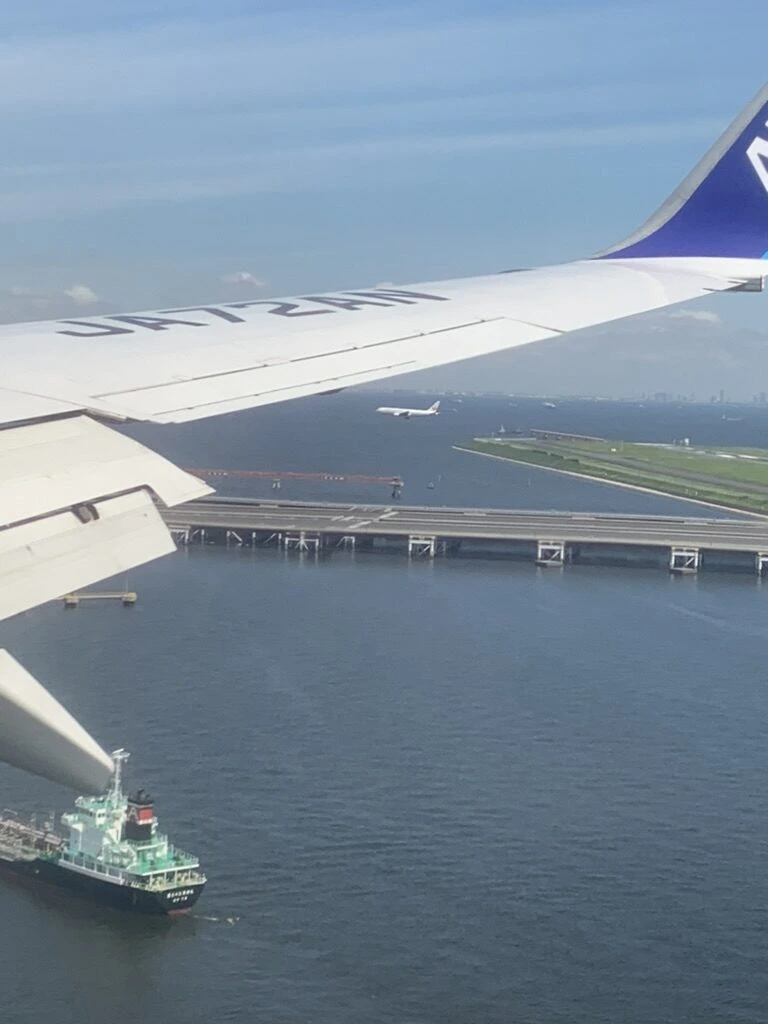 羽田着陸前のANA22便の機窓。海上の滑走路と、白い波を立てて進む船