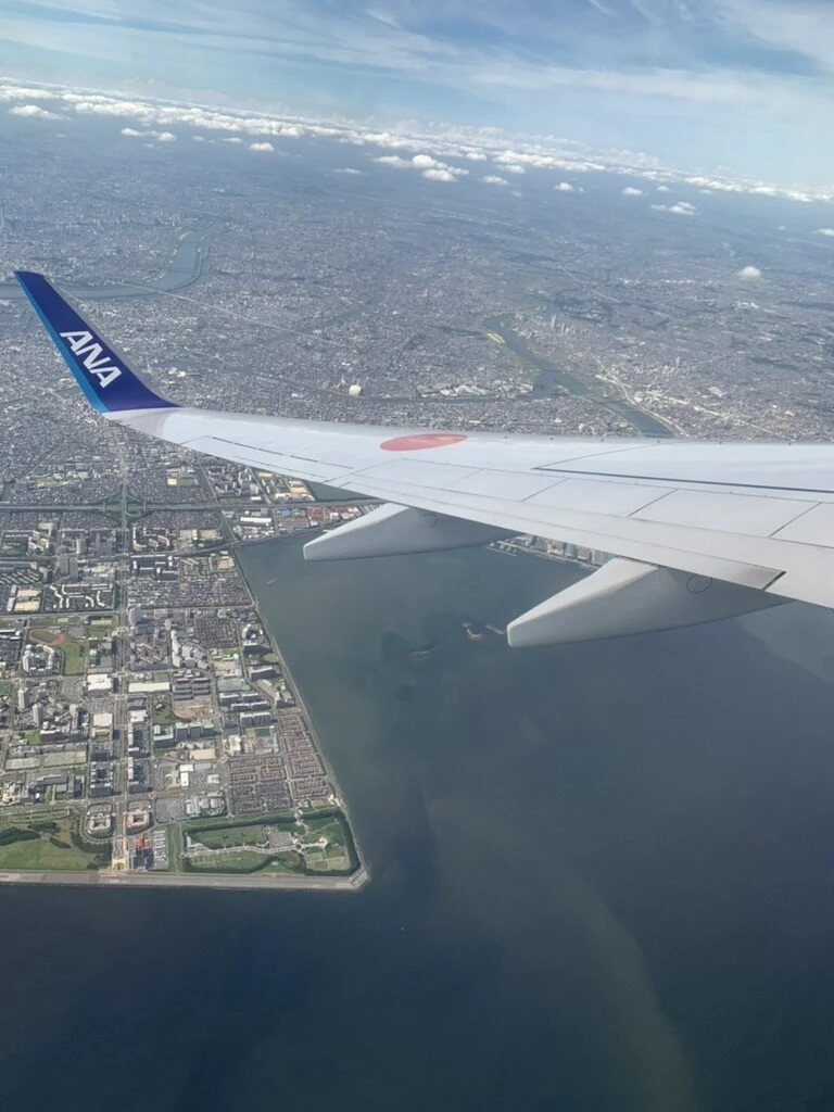 羽田を離陸したANA721便の機窓。主翼の下に東京湾岸の埋立地