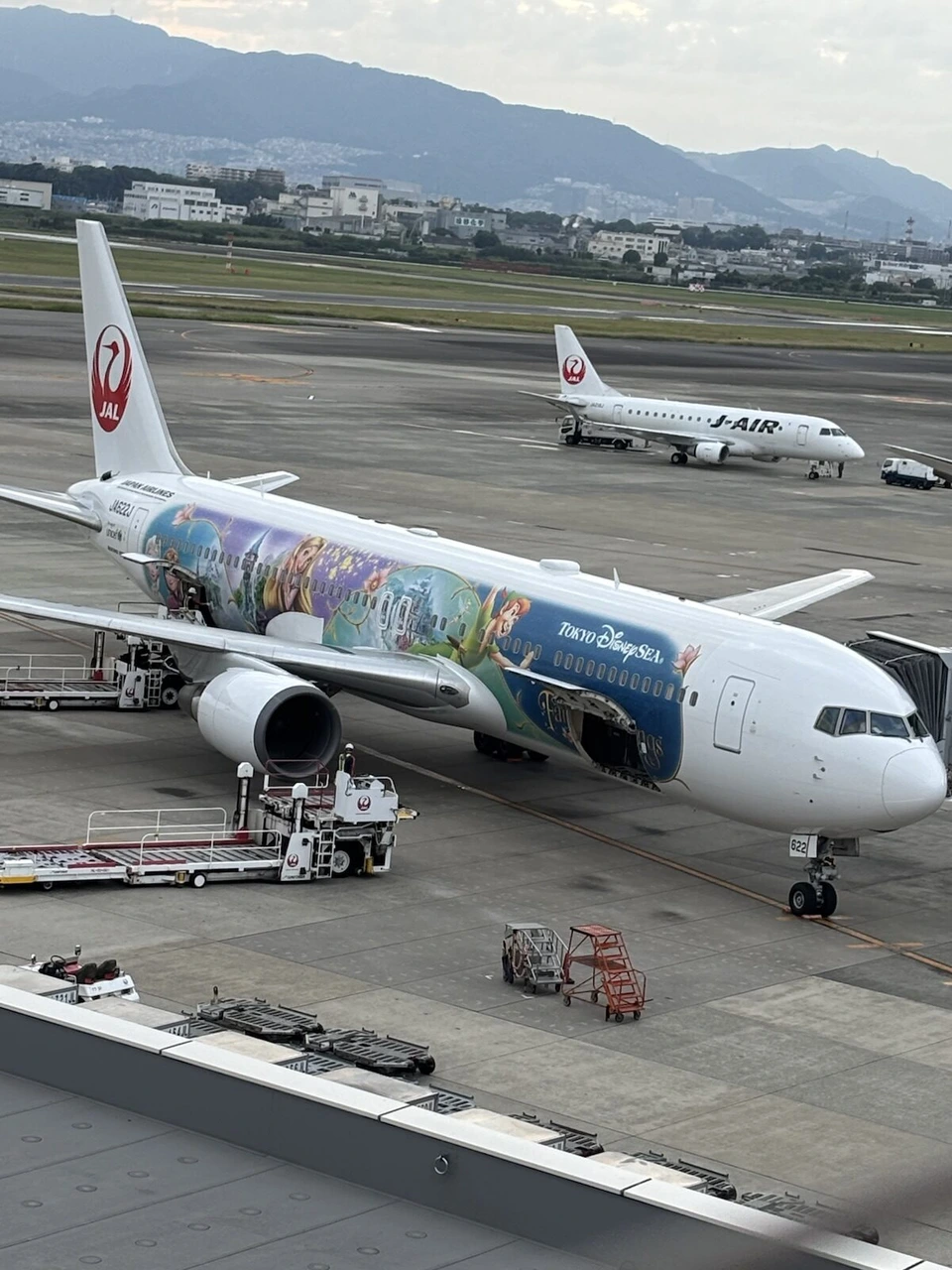 伊丹空港に駐機中の東京ディズニーシー塗装のJALボーイング767と、奥を走るJ-AIRのエンブラエル機