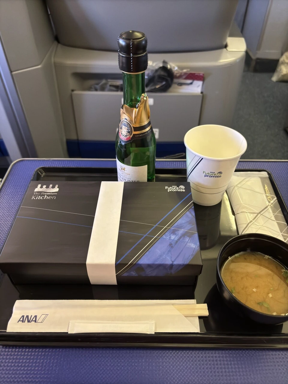 NH510 プレミアムクラスのトレー。The Premium Kitchenと書かれた黒い弁当箱、味噌汁、紙コップ、スパークリングワインの小瓶