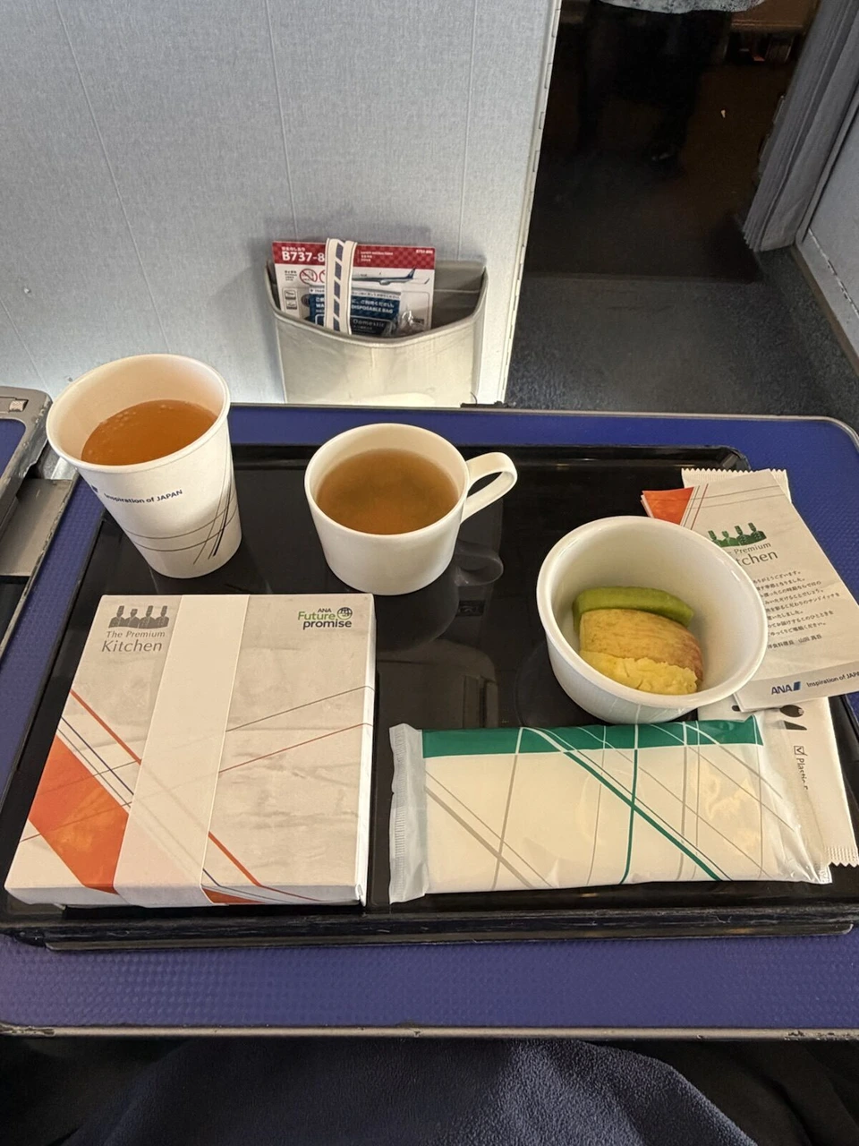 ANA NH577 プレミアムクラスのトレー。The Premium Kitchenの箱、スープ、紙コップの飲み物、小鉢、おしぼり