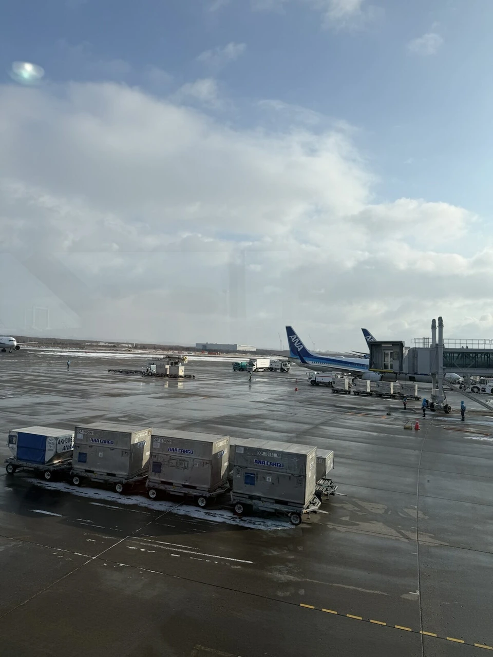 12月の新千歳空港の窓から見た雪の残る駐機場とANA機、コンテナ