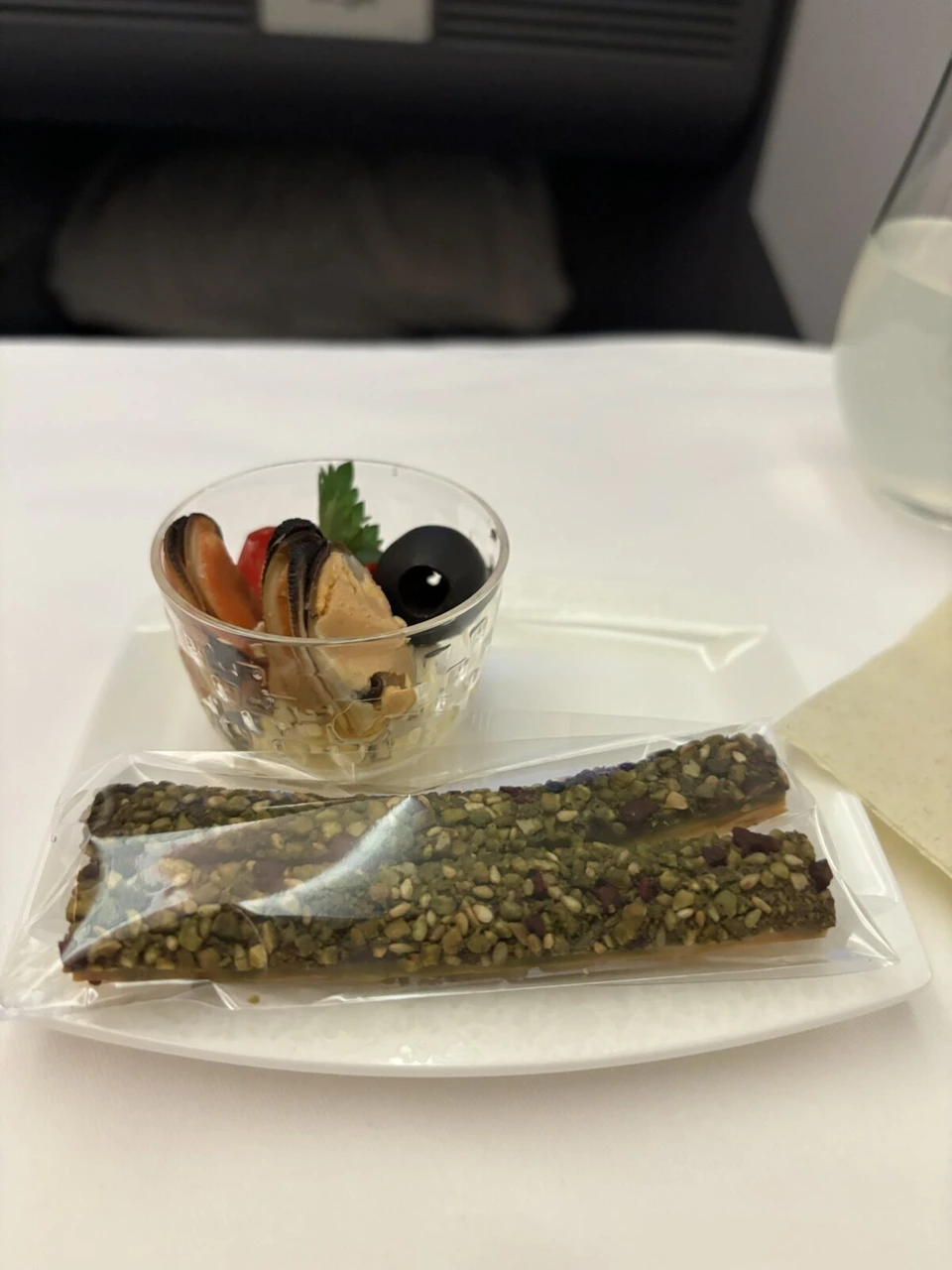 NH801ビジネスクラスのアミューズ。ムール貝などが入ったグラスと、種が載った細長いクラッカー
