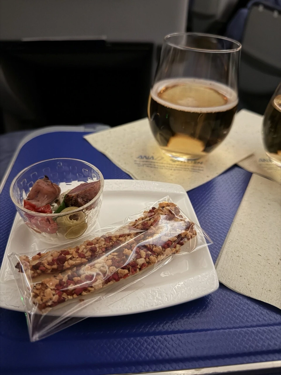 ANA NH885ビジネスクラスの機内食。グラスの飲み物と小さなサラダ、袋入りのスナックバー