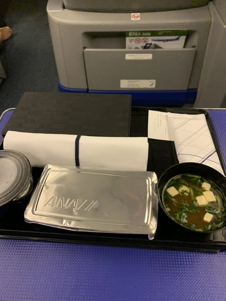 NH478 プレミアムクラスのふた付き機内食トレー。ANAロゴ入りの銀色のふたと味噌汁