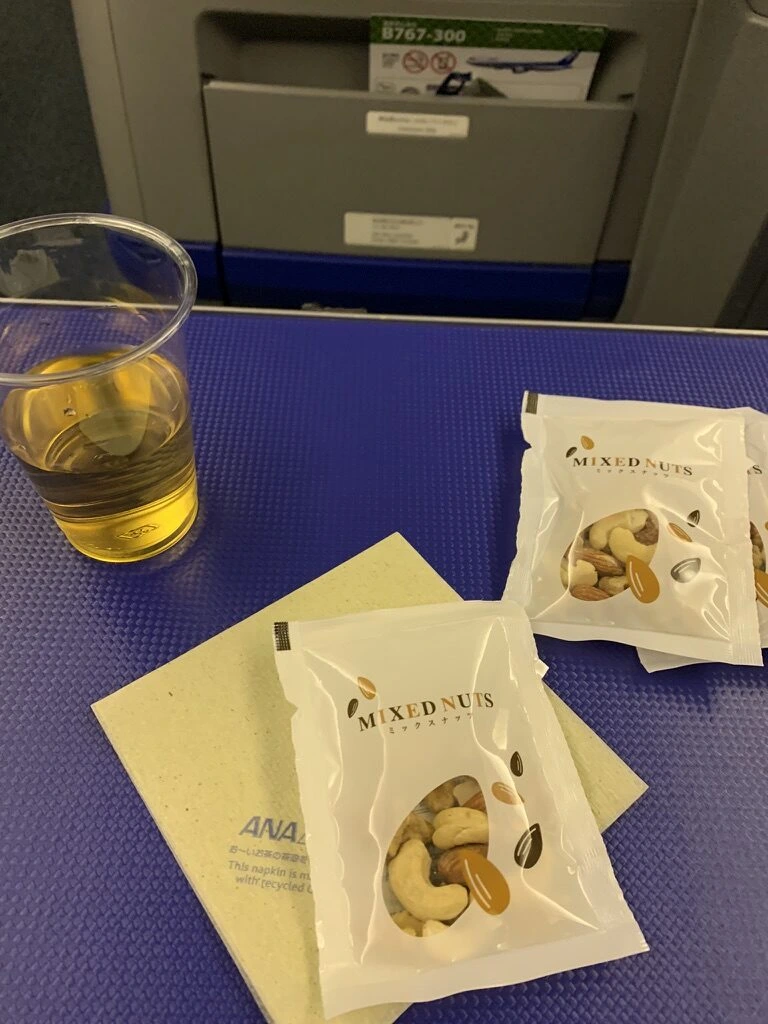 プレミアムクラスのミックスナッツの袋2つとカップの飲み物、ANAのナプキン