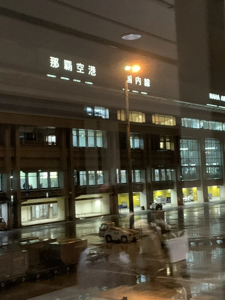 雨の夜の那覇空港。窓越しに那覇空港の文字とターミナル