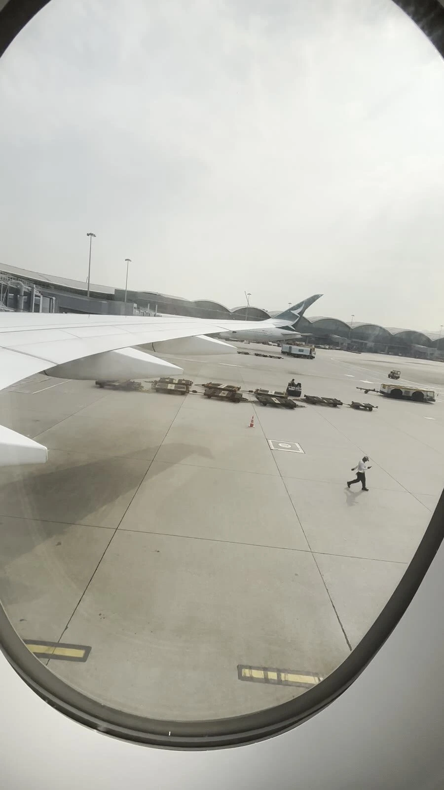 CX139の窓から見た出発前の香港空港の駐機場。主翼の先にキャセイパシフィックの尾翼と、地上の車両