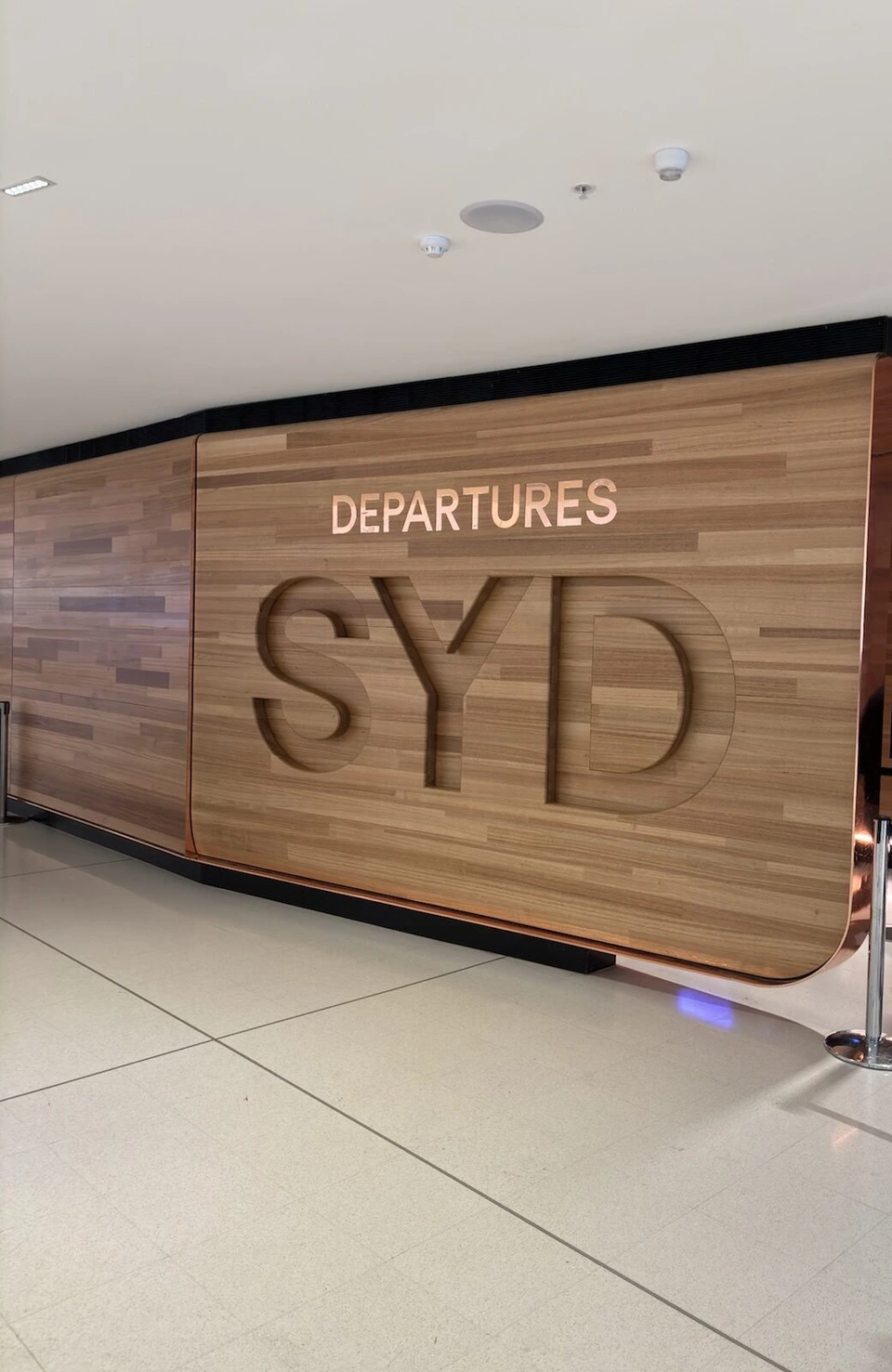 シドニー空港の出発エリア。木目の壁にDEPARTURES SYDの文字