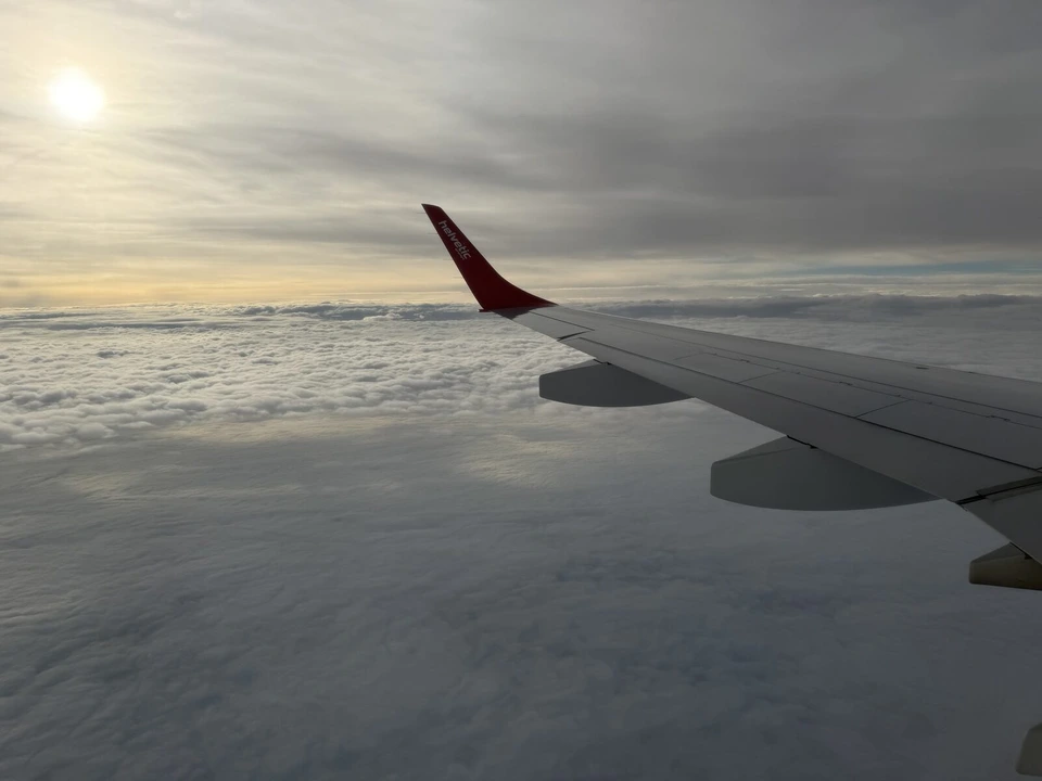 雲の上を飛ぶヘルベティック航空機の主翼と、雲の切れ間の太陽