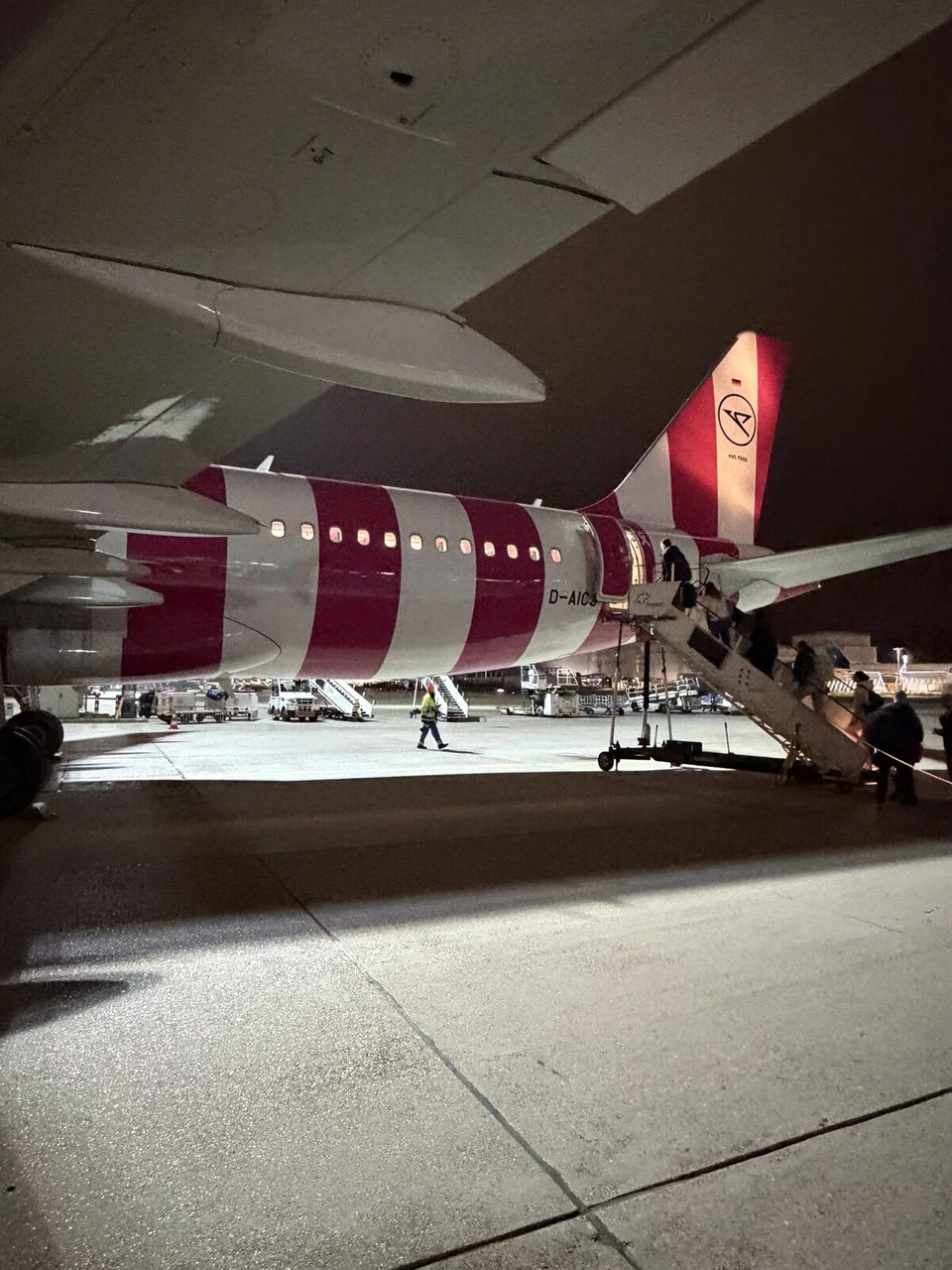 夜のフランクフルト空港で、赤と白のしま模様のコンドル航空A320に後ろのドアから乗り込む乗客