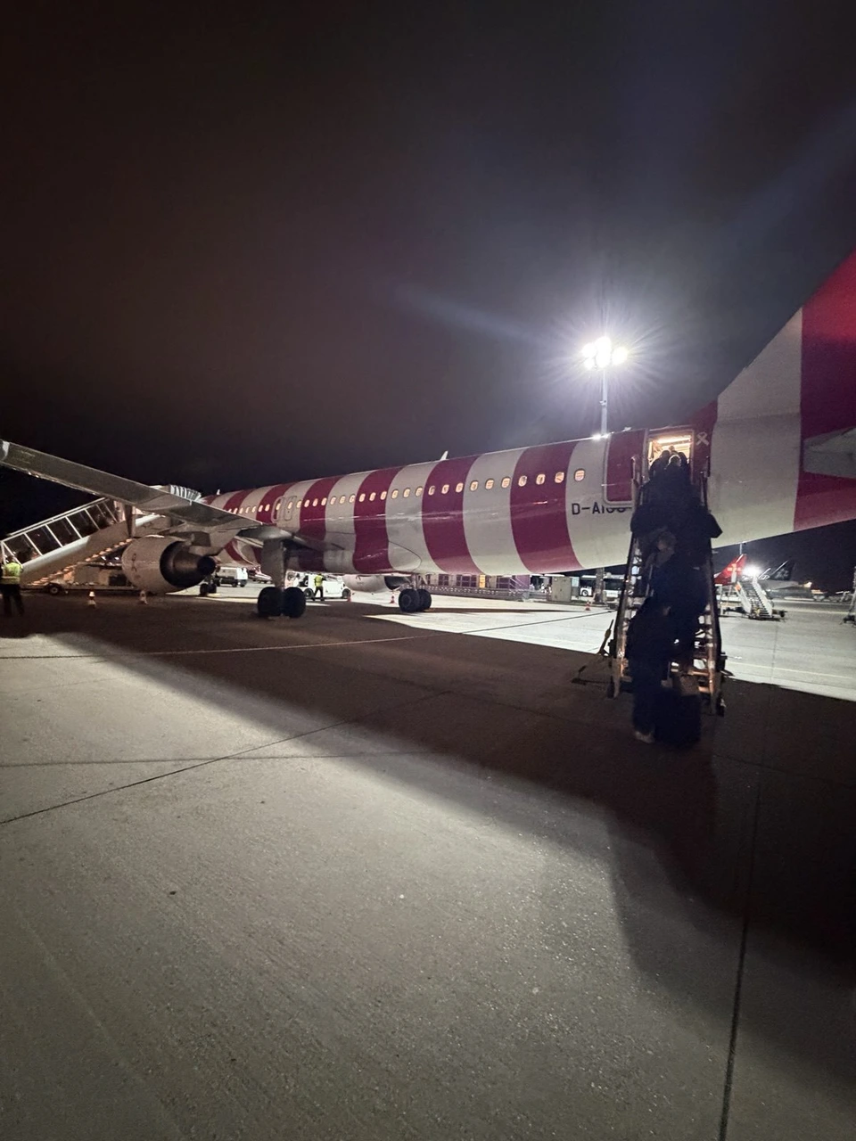 夜のフランクフルト空港の駐機場に止まる、赤と白のストライプのコンドル航空A320とタラップ