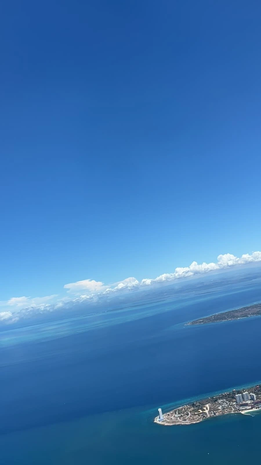 離陸後の機窓から見下ろした青い海と島の海岸線、遠くの雲