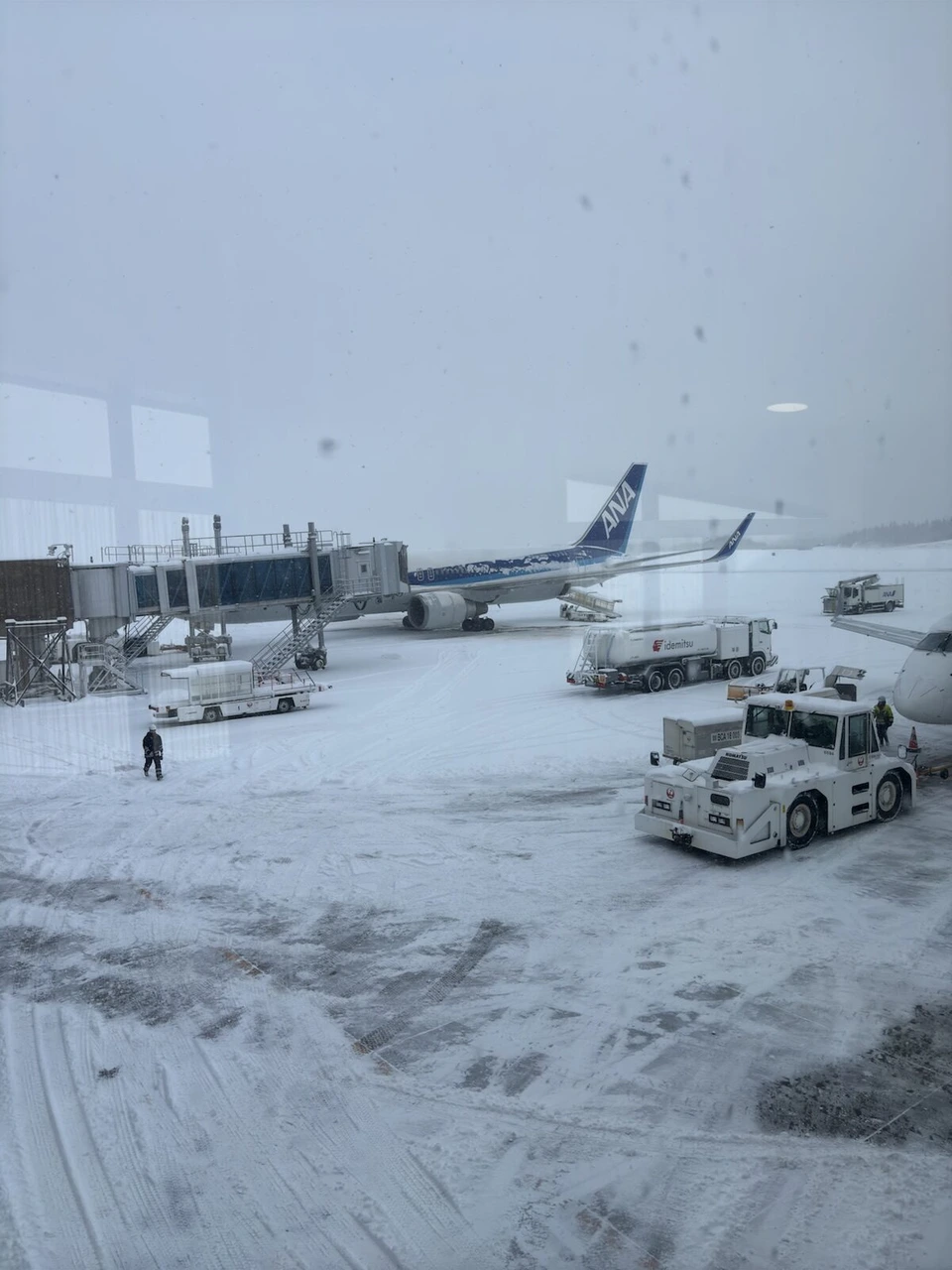 雪が降る秋田空港の駐機場。除雪車と雪に埋もれた機体