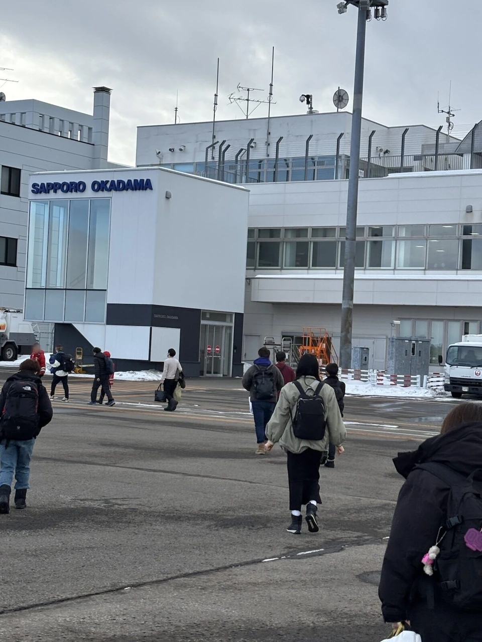 札幌丘珠空港の駐機場から、雪の残るターミナルへ歩く乗客の後ろ姿