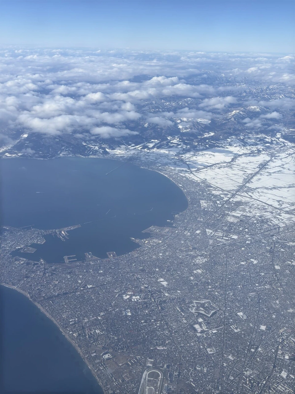 雲の切れ間から見下ろした、湾に面した雪の街