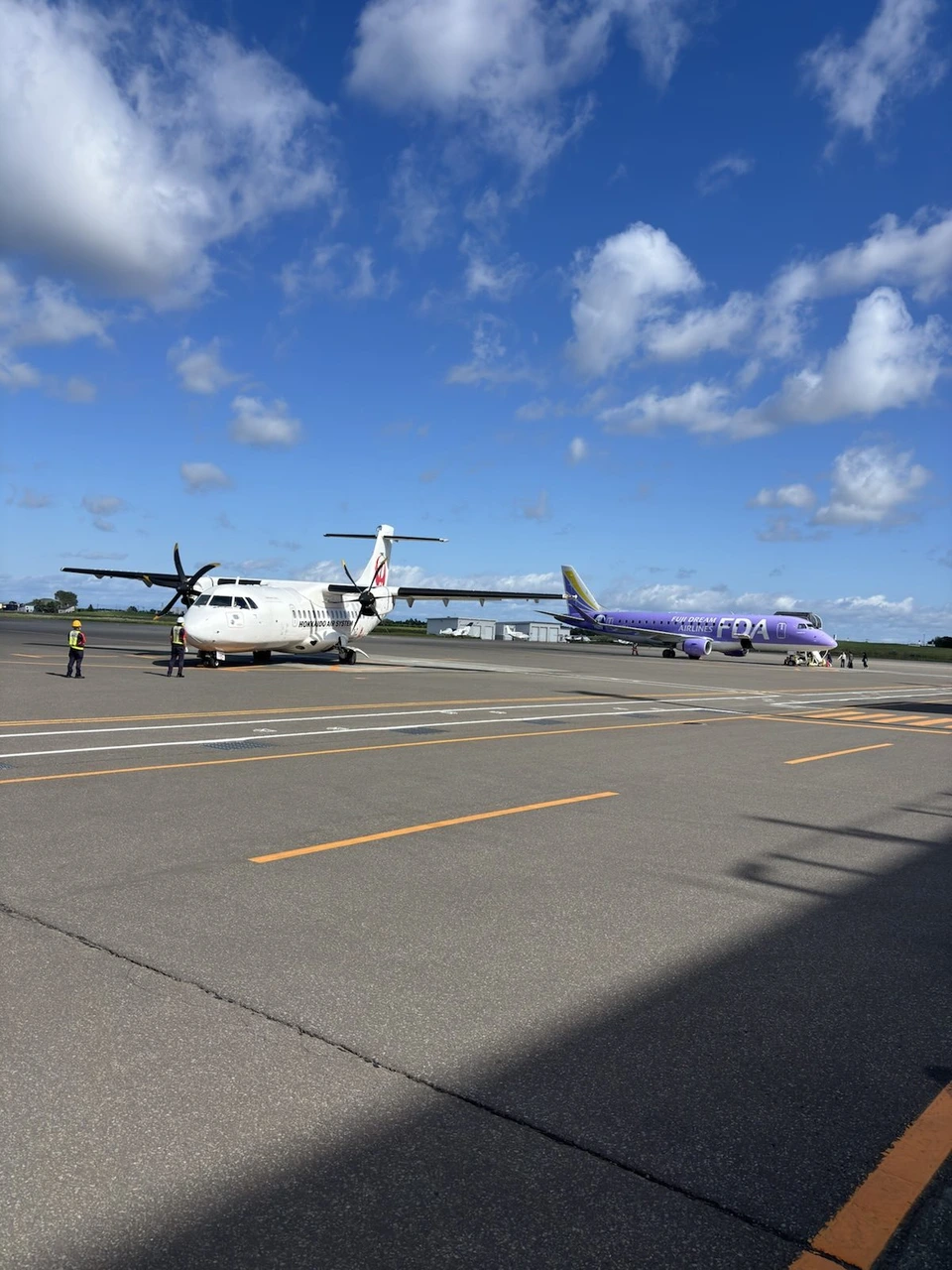 晴れた丘珠空港の駐機場に止まるJALのATR42-600。奥には紫色のFDAの機体