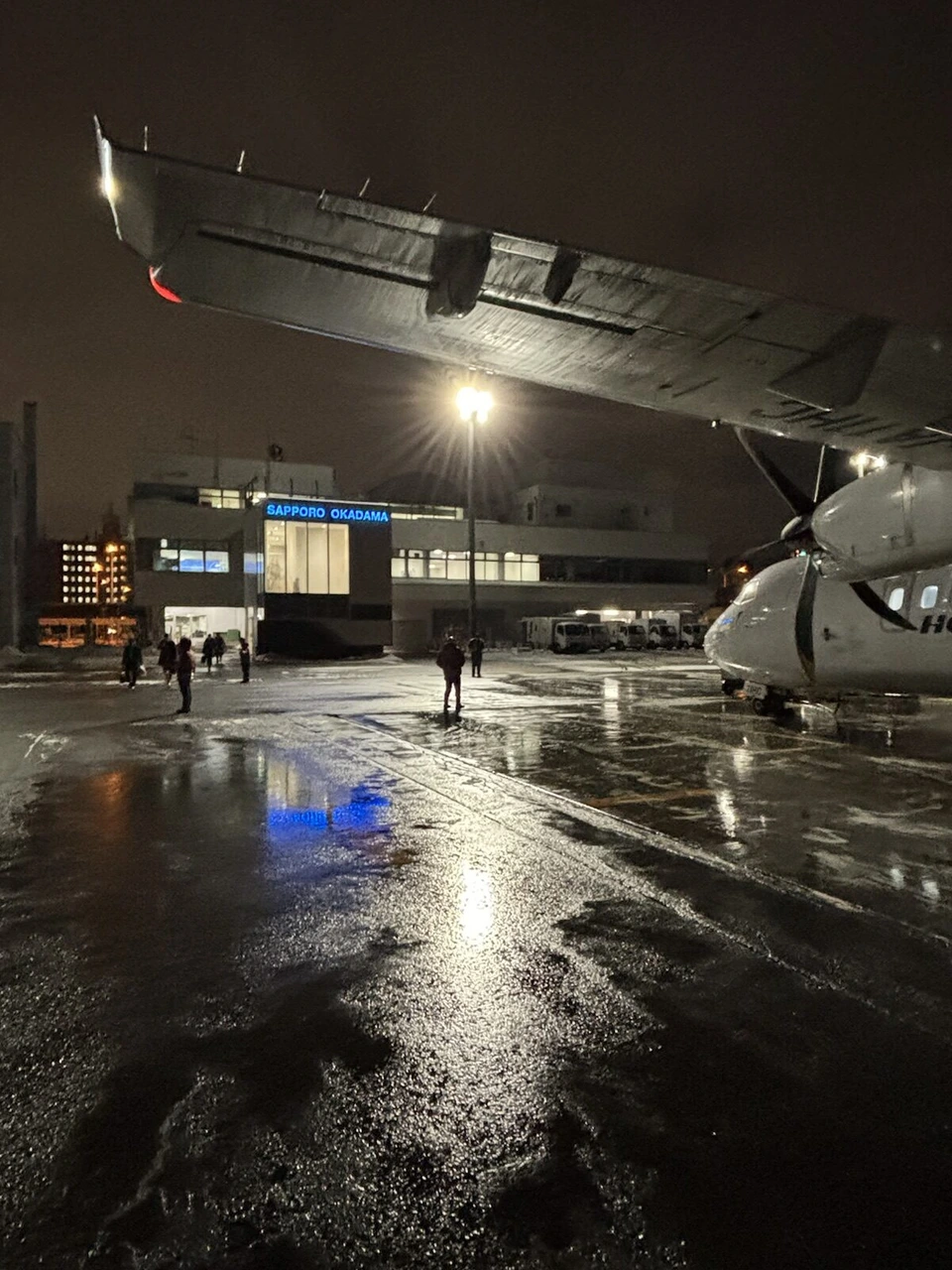 ATRの主翼の下から見た夜の丘珠空港のターミナルと、濡れた駐機場