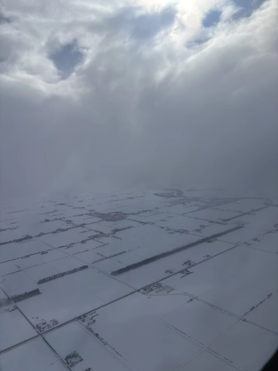中標津から丘珠へ戻るJL2732の機窓から見た、雲の下に広がる雪の平野と区画された畑