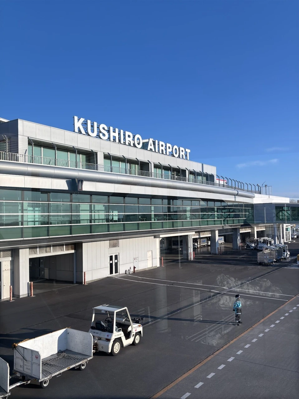 青空の下の釧路空港のターミナル。KUSHIRO AIRPORTの文字と駐機場の車両