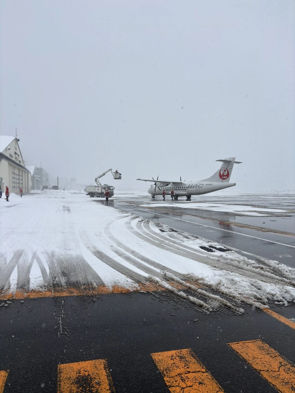 雪が降る丘珠空港で、除雪車のそばに止まるATR42-600