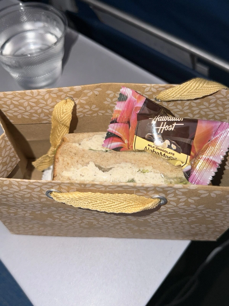 ハワイアン航空の機内の軽食。紙袋のサンドイッチとHawaiian HostのAlohaMacs、水