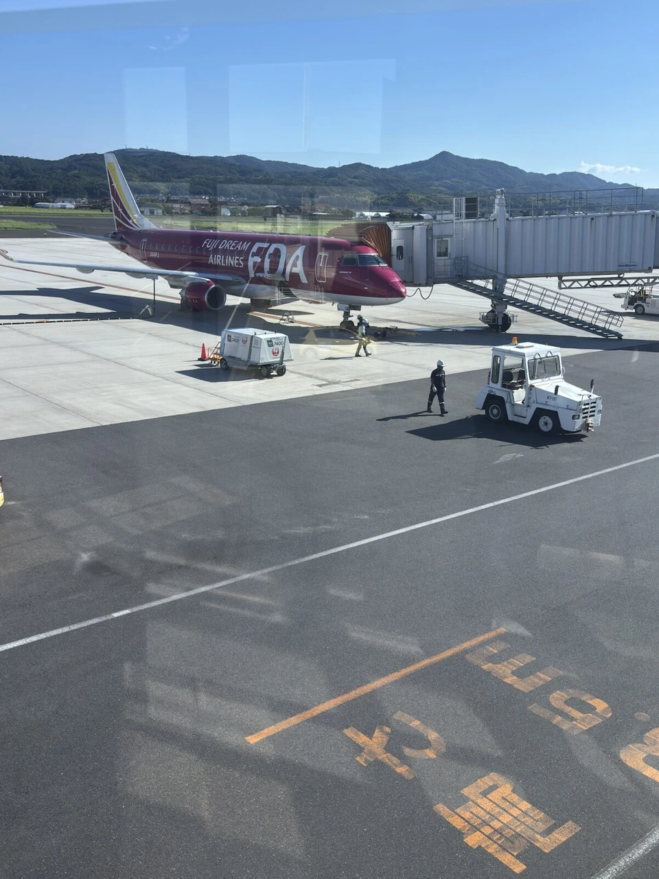 出雲空港の駐機場。ボーディングブリッジにつながるピンクのFDAの機体と地上の車両