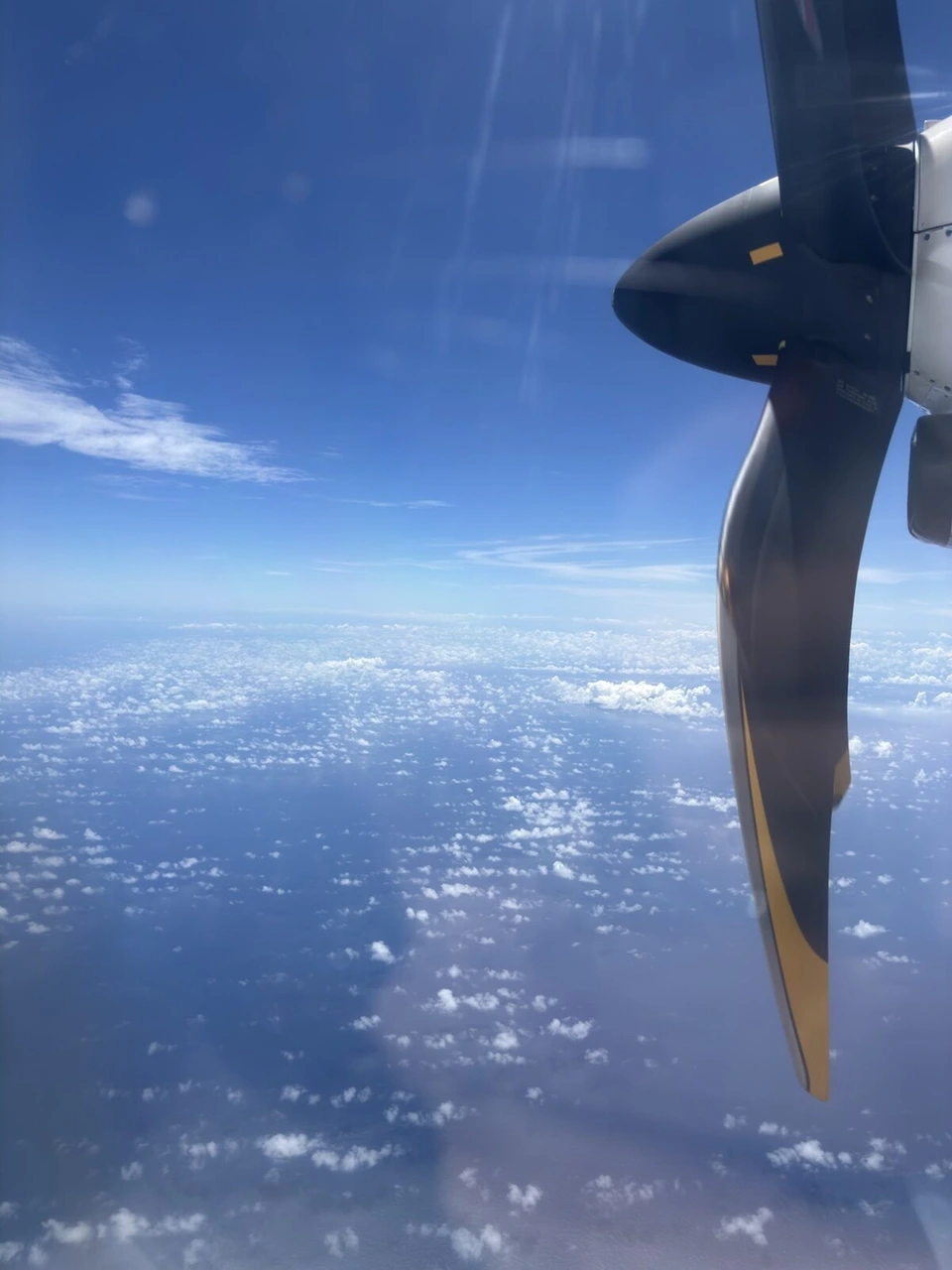 JL3785(ATR42-600)の窓から見たプロペラと、トカラ列島付近の雲の浮かぶ青い海