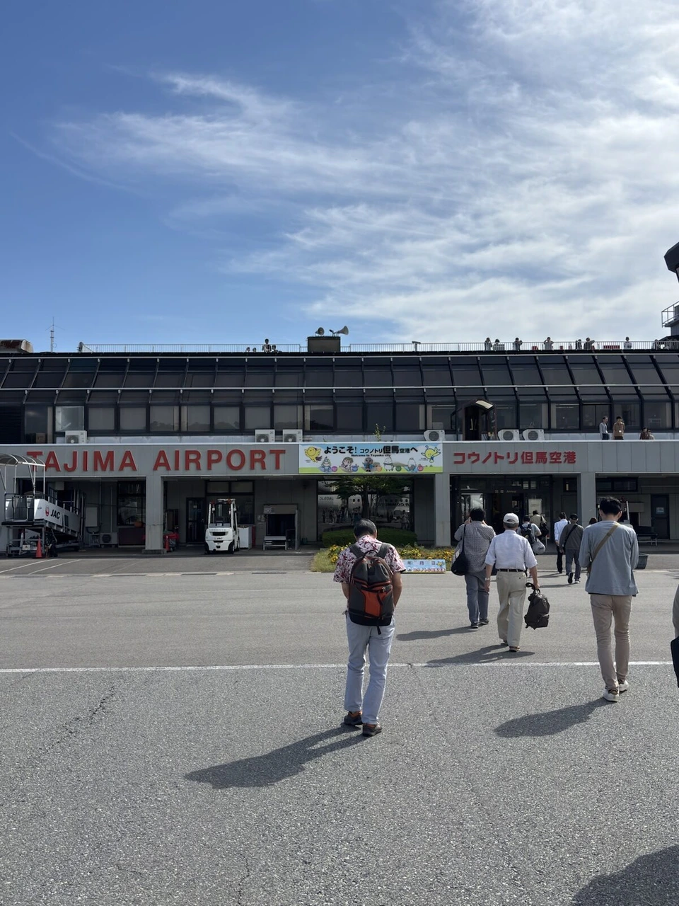 コウノトリ但馬空港の駐機場からターミナルへ歩く乗客。建物にTAJIMA AIRPORTの文字