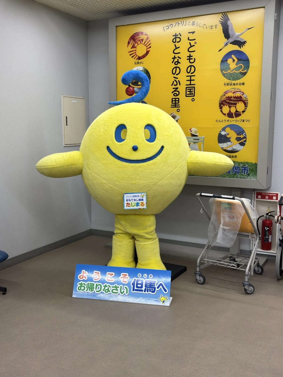 但馬空港の到着ロビーに立つ黄色いキャラクターたじまると、ようこそお帰りなさい但馬への看板