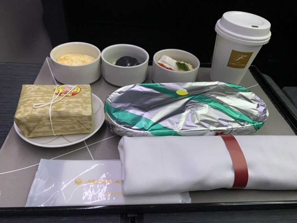 JL920のファーストクラスの夕食トレー。メインはアルミのふた付き、小鉢3つ、俵御飯、ナプキン、Fロゴのコーヒーカップ