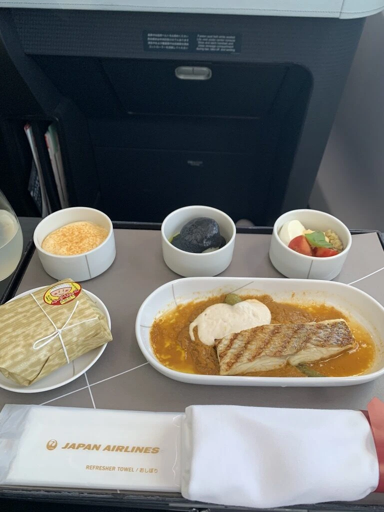 JAL国内線ファーストクラスの夕食。真鯛のグリル、小鉢3つ、竹皮風の包みの俵御飯、JALのおしぼり