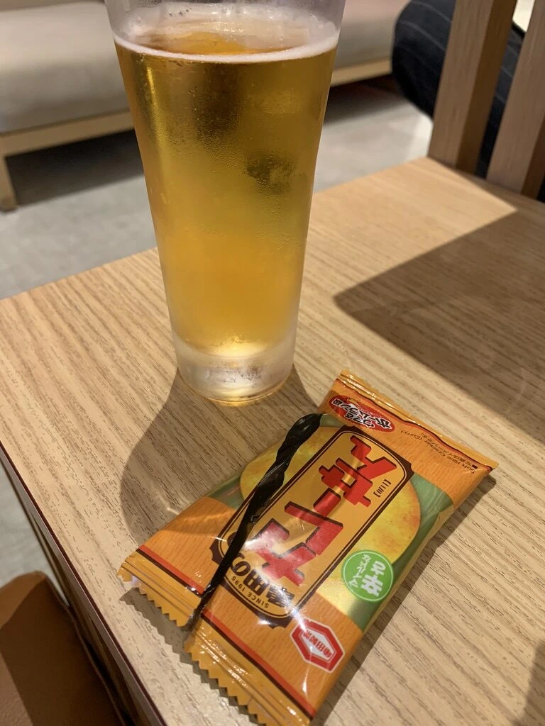 那覇空港のJALラウンジのテーブルに置いた生ビールとおつまみの袋