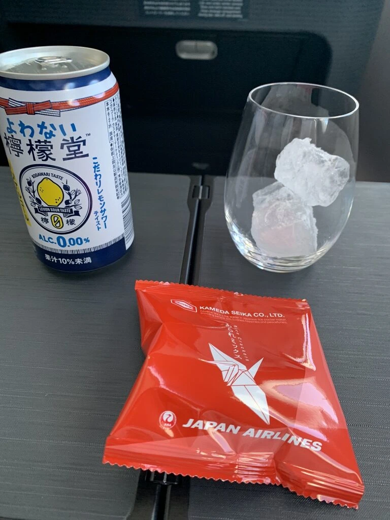 JL914ファーストクラスの飲み物。ノンアルコールのよわない檸檬堂の缶と氷入りのグラス、JALの赤い袋のおつまみ