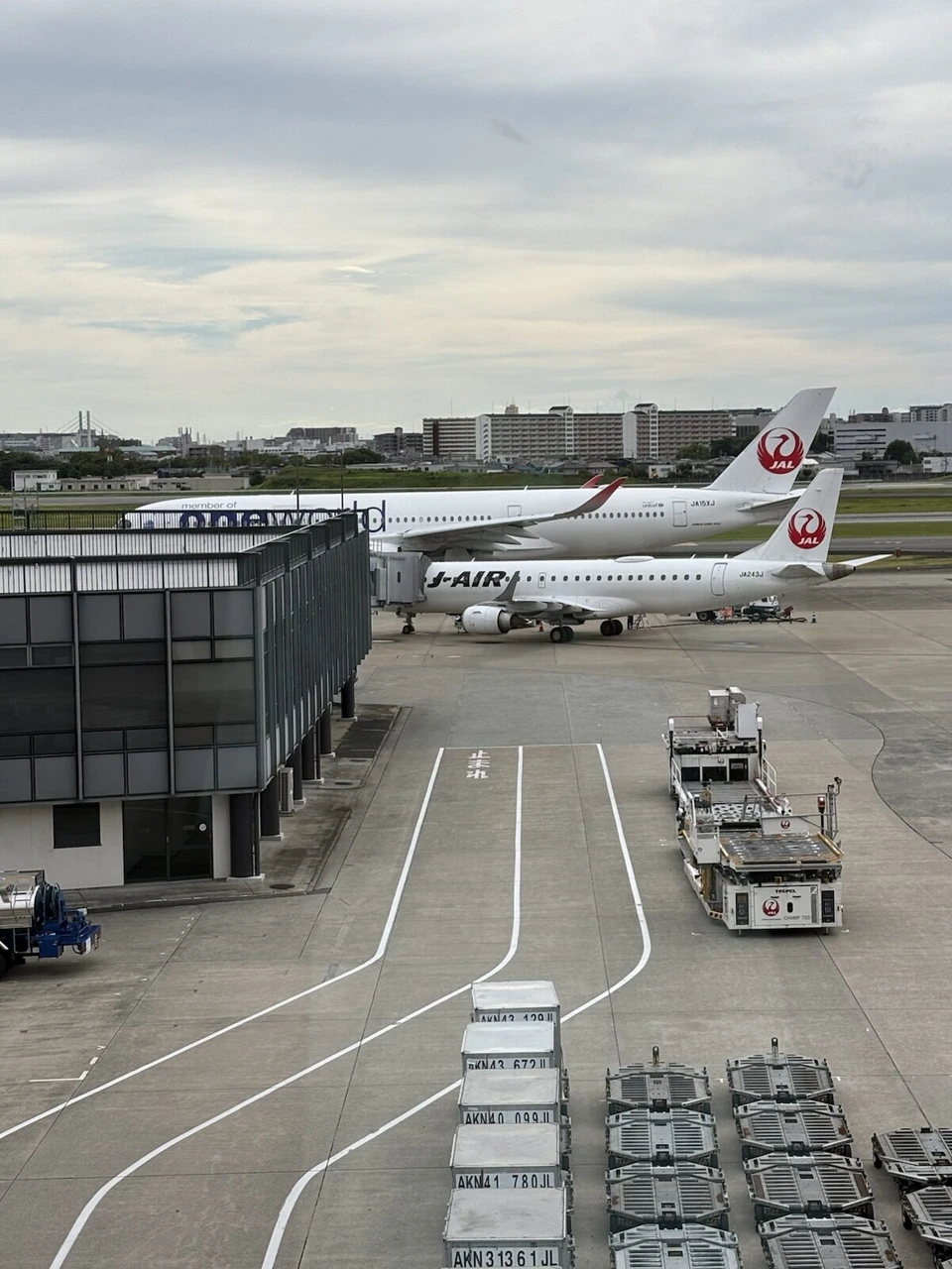 伊丹空港の駐機場に並ぶJALの機体とJ-AIRのE190、手前にコンテナ
