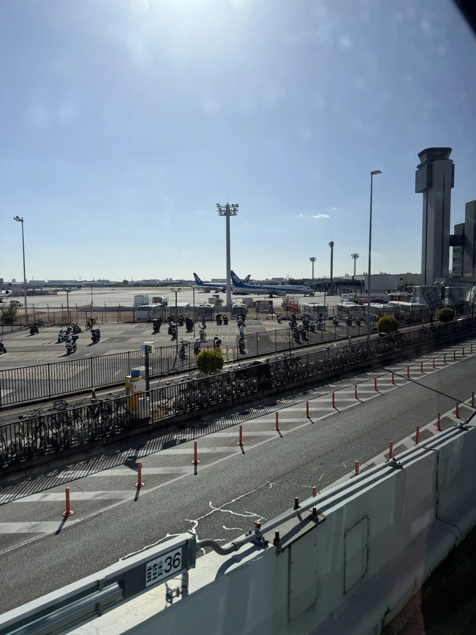 伊丹空港に着く手前の窓から見た、晴れた空の下の駐車場と管制塔、奥に並ぶ飛行機