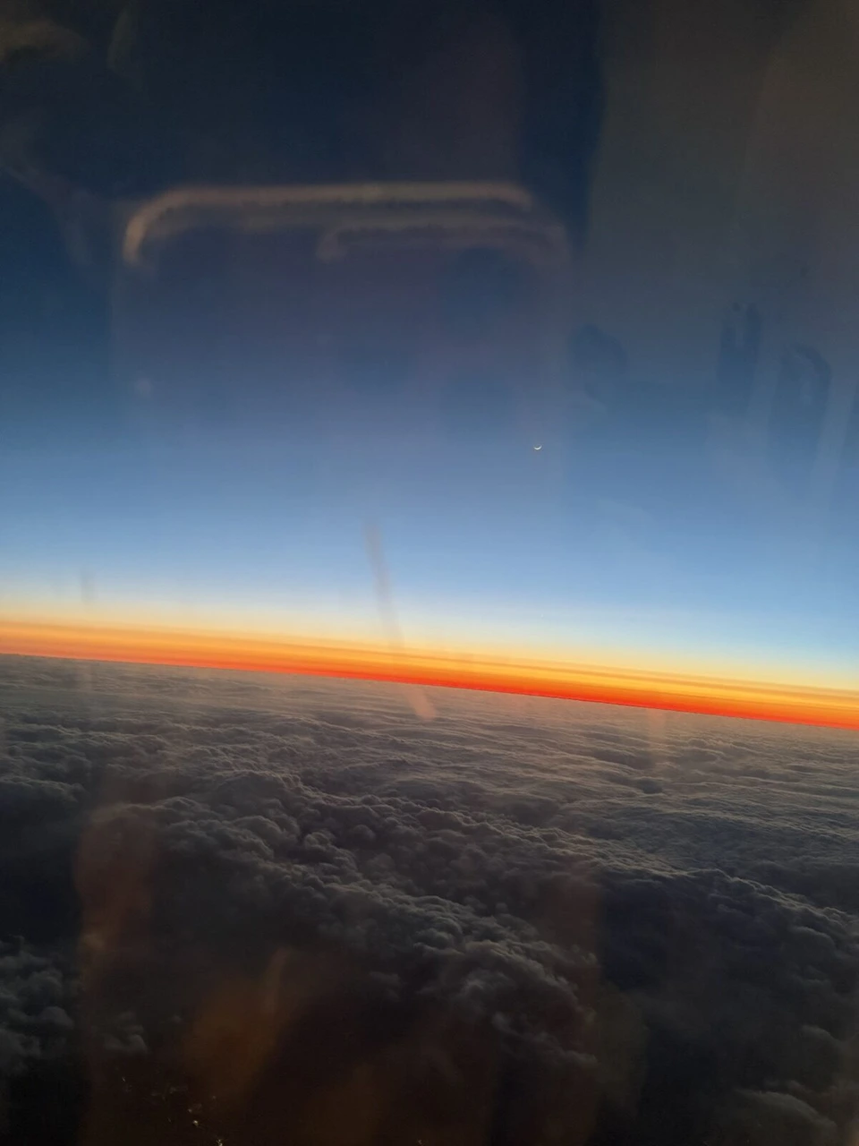 JL2907の窓から見た雲の上の夕焼け。地平線にオレンジの帯、上は青い空、下は暗い雲