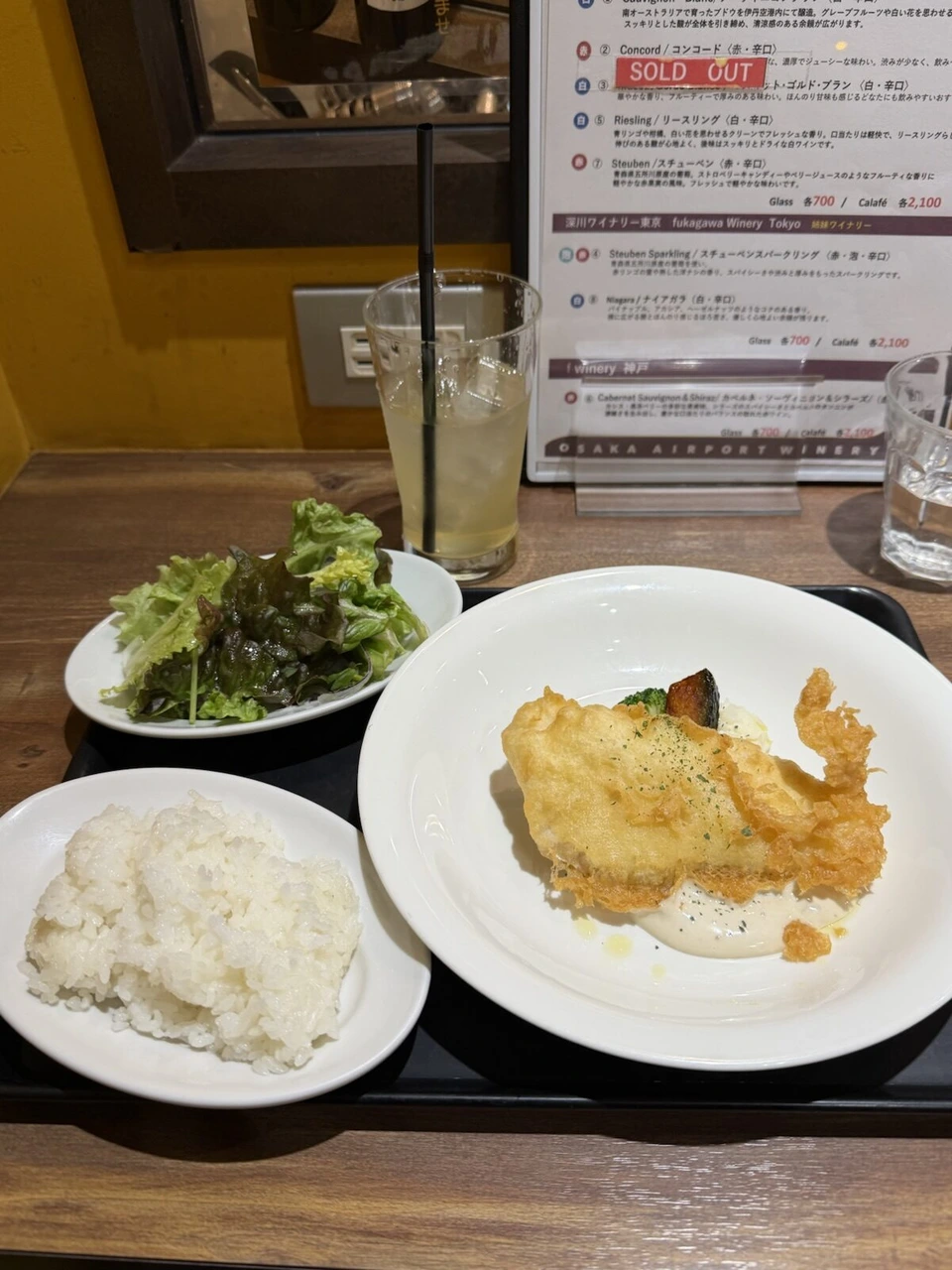 伊丹空港の店で食べたお昼。白身魚のフライにクリームソース、ごはんとサラダ、奥にワインのメニュー