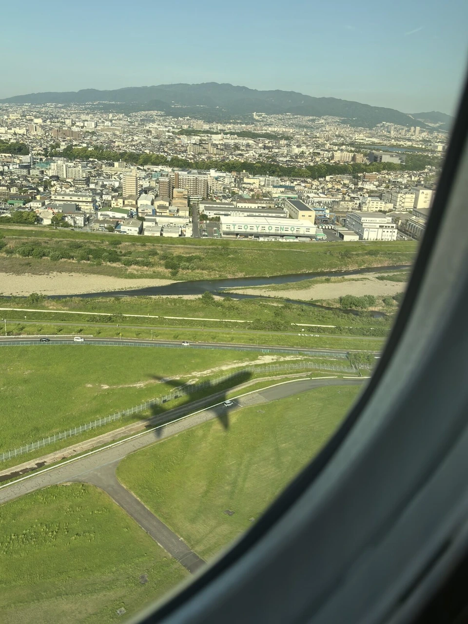 JL102の離陸直後の機窓。伊丹空港近くの河川敷に機体の影が落ちている